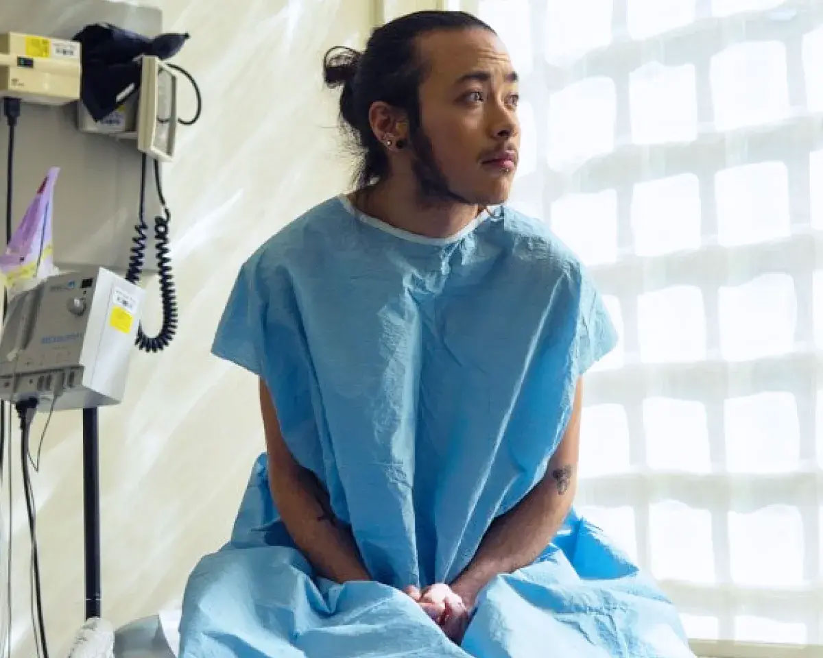 Male patient sitting in a hospital gown looking out the window