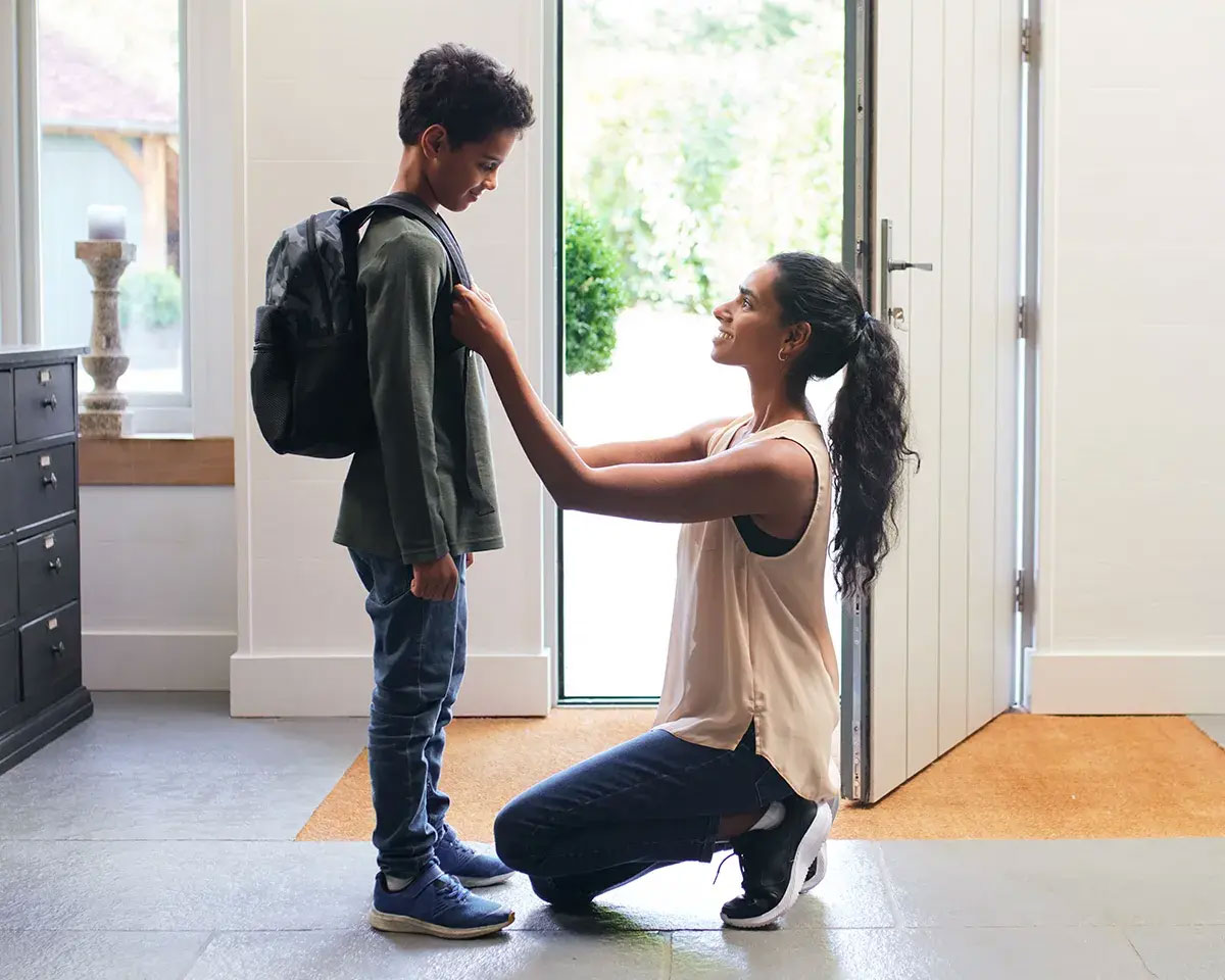 Women kneeling in front of her son helping him with his backpack